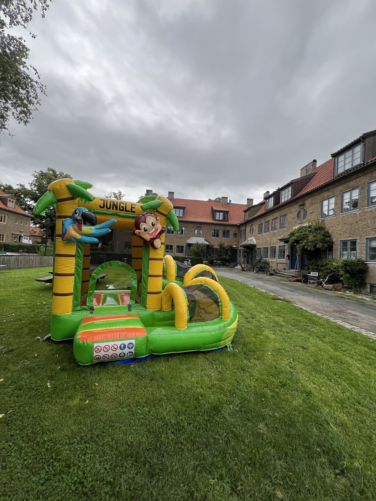 Grønt og gult jungel-hoppeslott på en gressplen i en bakgård mellom boligblokker