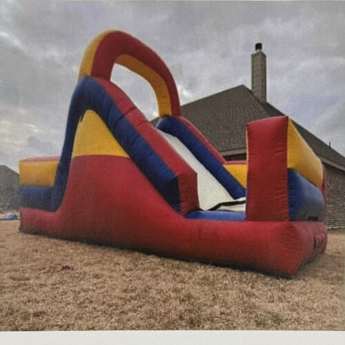 Colorful inflatable bounce slide on a grassy yard beside a brick house under a cloudy sky